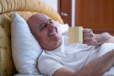 Pijamalı ve sabahları evinde yatarken kahve içen mutlu kıdemli adam..