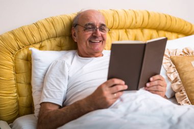 Gri saçlı, gözlüklü, yatakta kitap okuyan, evde sakin ve rahat bir sabah geçiren son sınıf öğrencisi. Boş zaman ve emeklilik yaşam tarzı.