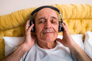 Yatak odasında kablosuz kulaklıkla müzik dinlemekten zevk alan mutlu bir son sınıf öğrencisinin yakın portresi.. 