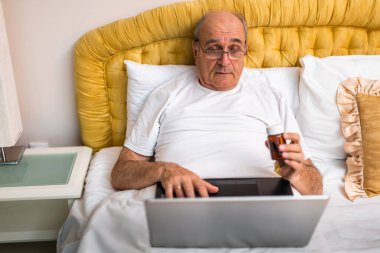 Son sınıf öğrencisi ilaç şişesini tutuyor ve yatak odasında yatarken bilgisayardan tıbbi bilgileri analiz ediyor.. 