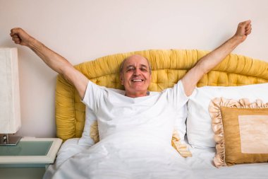 Yatakta yatarken kollarını kaldırarak esneten neşeli bir son sınıf öğrencisi. Gülümsüyor ve sabahı canlılık ve mutlulukla selamlıyor..