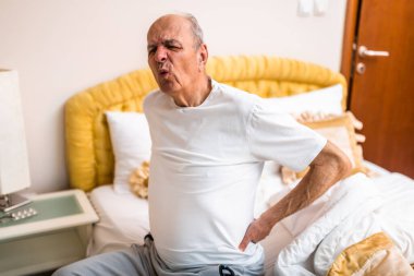 Yaşlı bir adam sabah uyanıp yatakta oturduktan sonra sırt ağrısı çekiyor. Yaşlanınca fiziksel yaralanma ya da kas gerginliğini temsil ediyor..