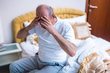 Sabah uyanıp, hafifçe aydınlatılmış yatak odasında yattıktan sonra baş ağrısı çeken yorgun yaşlı bir adam..