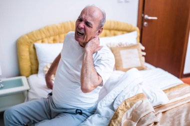 Buruşuk kıdemli adamın boynu ağrıyor. Sabah erken kalktıktan sonra yatakta otururken bağırıyor.. 