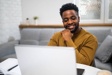 Afrikalı uzaktan kumandalı bir işçi, evinde otururken bilgisayarındaki video konferansı sırasında dinleyip iletişim kuruyor..