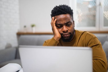 Endişeli Afrikalı Amerikalı iş adamı evinde çalışırken dizüstü bilgisayar kullanıyor..