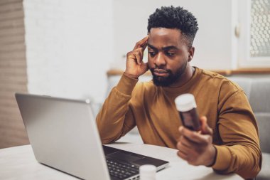 Evdeki teletıp danışmanlığı için dizüstü bilgisayar kullanan Afrikalı Amerikalı bir adam..