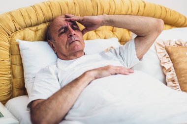 Depresyondaki yaşlı adamın sabah erken saatlerde yataktan kalktıktan sonra başı ağrıyor..