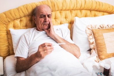 Son sınıf öğrencisi hasta yatağında yatıp ateşini ölçüyor ve nezle virüsü ya da gribi düşünüyor..