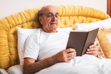 Rahatlamış kıdemli adam evinde dinlenirken kitap okuyor..