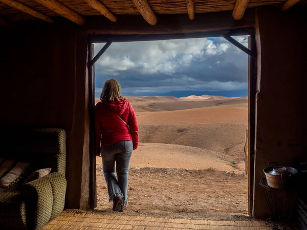 Woman next to the door of a Moroccan adobe house looking at the Agafay desert