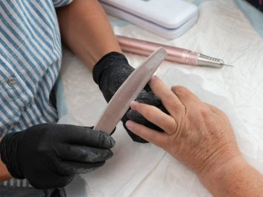 A woman is filing another woman's nails. The young woman is using a nail file to file the woman's nails. clipart