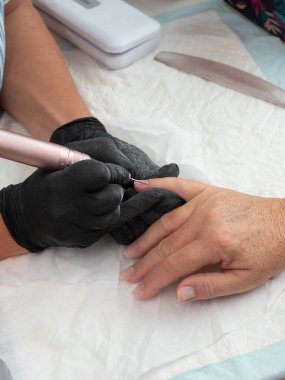 A manicurist is cleaning cuticle and paint residue from a woman's nails with an electric nail drill with flame burr clipart