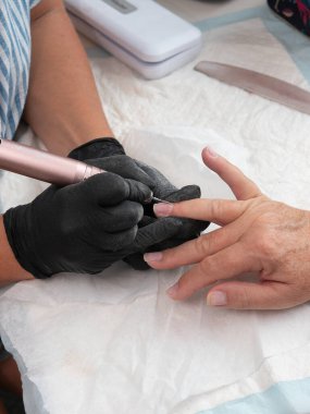 Bir manikürcü, bir kadının tırnaklarındaki kalıntıları ve boya kalıntılarını alev yanıklı bir elektrikli tırnak matkabıyla temizliyor.