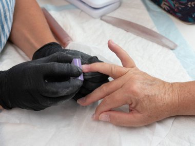 A manicurist files a woman's nails with a nail sanding sponge clipart