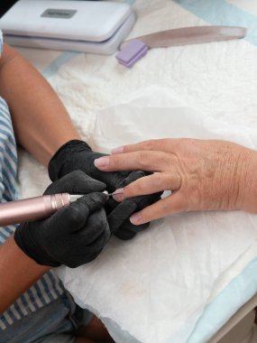 A manicurist is cleaning cuticle and paint residue from a woman's nails with an electric nail drill with a ball mill. clipart