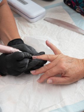 A manicurist is cleaning cuticle and paint residue from a woman's nails with an electric nail drill with flame burr clipart