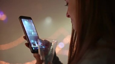 Güzel bir kadın cep telefonuyla gece sisli caddenin fotoğraflarını çekiyor. Güzel dekore edilmiş ve aydınlatılmış bir gece sokağı. Yılbaşı partisinde. Şenlikli fotoğraf akıllı telefondan çekildi, tatil havası konsepti.