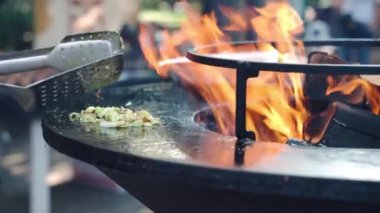 bbq sigara ızgarasında kızarmış soğan dilimleri, ateşte kızartılmış sebzeler. Izgara yaparken soğan dilimlerini karıştırmak için bbq maşası kullanan profesyonel barbekü içicisi ve yanan