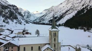 İsviçre dağlarında güzel bir kış, küçük turistlerin üzerinde uçan insansız hava aracı Alpler 'in ortasında köyler, eski kilise ve karla kaplı geleneksel İsviçre dağ evleri.