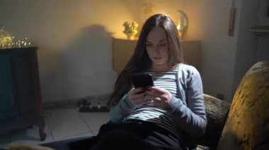 Smartphones and online virtual reality being a problem of modern society, woman sitting in armchair and using cellphone, female browsing internet, reading news and showing surprised emotions. Young