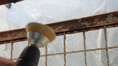 Metal fırça başlıklı elektrikli öğütücü, bir açıyla dönüyor ve metal yüzeydeki paslı boyayı söküyor. İnşaat alanındaki çeliğin üzerindeki ağır aşınmayı kaldırıyor. İşçi temizliği