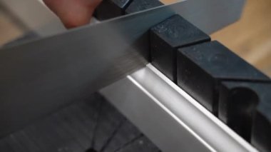 İşçi keskin bir el testeresi ile ölçülmüş beyaz plastik deste kesiyor. Erkek, kurulum için süpürgelik hazırlıyor. Plastik etek tahtasını testere ile kestikten sonra beyaz talaş, tamir işleri