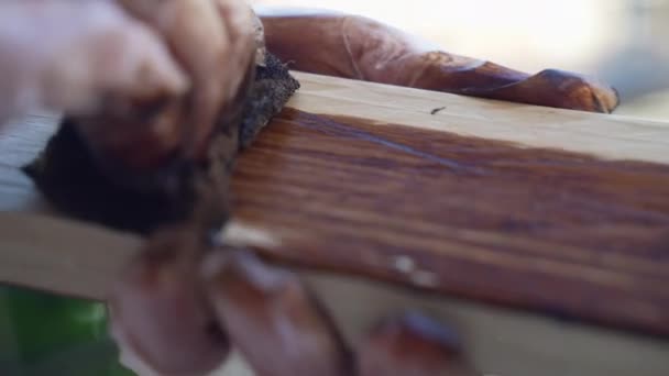 车间里 木匠戴着防护手套 用原木木板工作 用褐色油基油漆覆盖木材表面 以防止天气破坏 并制作家具产品 — 图库视频影像