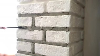 İnşaat alanındaki son onarımlar, beyaz taş kiremitlerle dekore edilmiş sütun duvarı, harç döşemeli duvar eklemleri gruplandıran işçiler. Dekoratif yüzey dokusu düzleştiriliyor