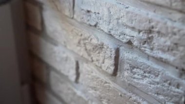 İnşaat alanındaki duvarda beyaz süslemeli taş, eldivenli işçi yumuşak endüstriyel fırça kullanarak taş kiremitleri beyaz renkte boyuyor, iç dekorasyon çalışmaları, ev geliştirme konsepti.