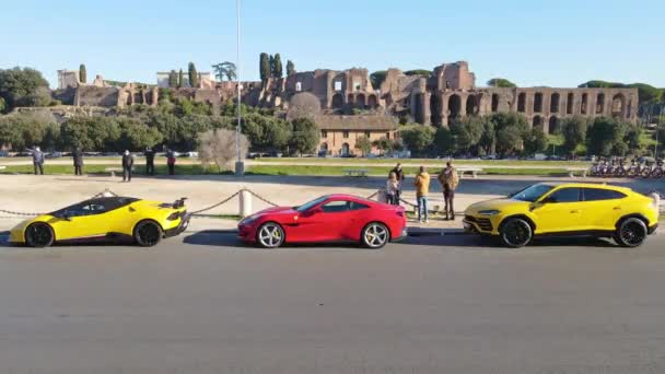 ローマ イタリア 2022年11月7日 Fori Imperaliを背景に話をする裕福な友人のグループと排他的なスポーツカー 黄色のランボルギーニと赤フェラーリを駐車しました — ストック動画