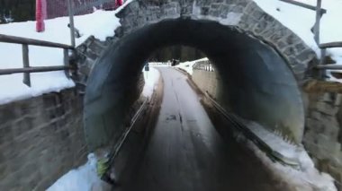 İnsansız hava aracı orman yolunda küçük dar bir tünelde uçuyor ve karla kaplı Alp dağlarının muhteşem manzarasını turistler ve ekstrem sporlar için kış beldesi,
