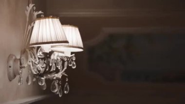 Duvarında kumaş abajur ve kristal kolyeler olan gümüş bir şamdan karanlık odayı aydınlatan, rahat bir akşam atmosferi için zarif bir iç mekan, duvarda klasik bir avize asılı. Yüksek kalite