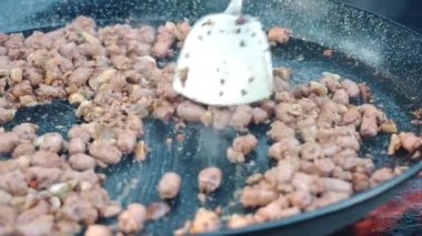 Büyük bir ızgara kazanda ateşte kızaran saustik sosisleri kes, kızarmış yemekleri bbq spatula ile karıştıran adam, cızırdayan yağda kızaran yiyecek. Sokak ya da abur cubur pişirme, hafta sonu piknik konsepti. Yüksek