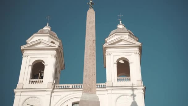 青い空の背景 伝統的なイタリアの文化や古代の建築に対する2つの小さなドーム 教会の鐘と高い宗教的なオベリスクを持つ建築トリニータ モンティ教会 — ストック動画