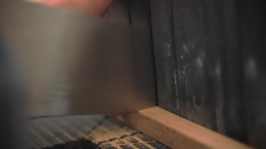 Elle testereyle çiğ tahta kesen bir adam, tahta keserken uçan bir toz görmüş. Atölyede ahşap malzemelerle çalışan bir adam yüksek kaliteli mobilya ve ürünler üretiyor.