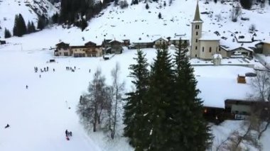 İsviçre Alp Dağları 'nın göbeğinde antik kilise kulesi olan turistlerin hava manzarası, dışarıda dinlenen insanlar, ev ve kulübelerin yakınında kayak ve kızak yapmak, İsviçre' deki kışlık tatil köyü.