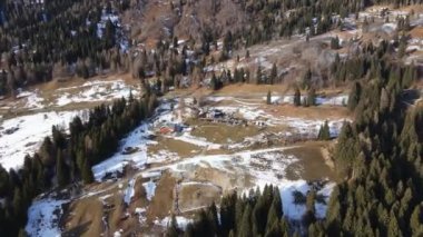 Güzel çam ağaçlarının gökyüzü manzarası güneş ışığı altındaki orman manzarası, karla kaplı görkemli İsviçre Alp dağları, ahşap kulübeler, dağ evleri ve turistler için ormanın göbeğindeki evler.