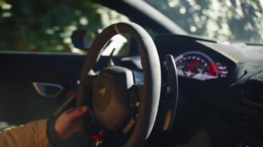 Unrecognisable driver steering wheel of sports car with powerful motor engine, view from inside of driving car in slow motion, illuminated modern dashboard as a part of trendy interior design. High