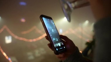 Switched camera mood on smartphone in hands of happy young woman drinking sparkling champagne against amazing illuminated festive background, female taking pictures of night streets decoration on