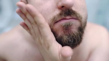 Facial skin redness and irritation as a result of daily dry shaving, man smoothing his beard with emollient oil in front of the mirror, facial procedures and skin care treatment at home, guys