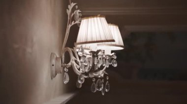 Vintage metal sconce with fabric lampshade and crystal pendants on the wall illuminating dark room, elegant old-fashioned interior detail for cozy evening atmosphere, retro chandelier hanging on the