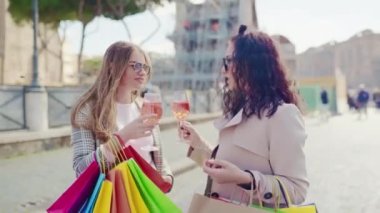 Female friends meeting in the city centre and drinking refreshing aperol spritz cocktail after perfect shopping day, smiling ladies talking and flirting on camera, stylish women with colourful