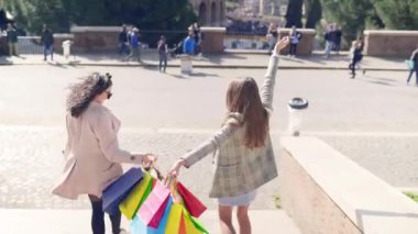 Stylish flirting female friends walking in the city centre with colourful shopping bags, women enjoying weekend relaxing in the shopping mall and fashion boutiques, female shopaholic concept. High