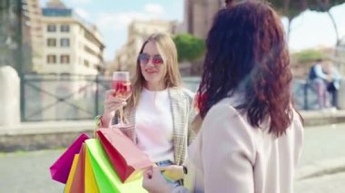 Glamour female friends meeting in the city centre and drinking refreshing aperol spritz cocktail after perfect shopping day, smiling ladies talking and flirting on camera, stylish women with colourful