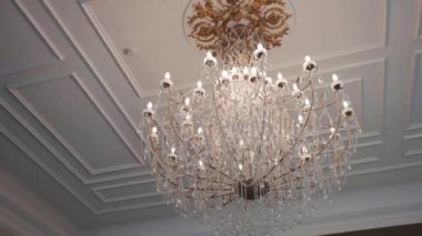 Luxury Victorian style chandelier hanging on ceiling ornate with gold, lightbulbs illuminating room, crystal pendants decorating vintage chandelier. Retro hanging lamp in palace hall, museum room or