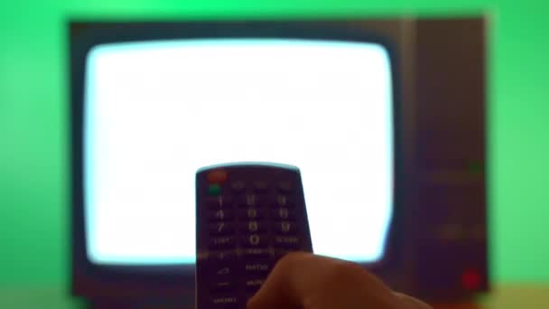 リモートコントロールを保持し ヴィンテージテレビ 緑の背景に古いテレビでチャンネルを変更する人 点滅ストライプとテレビディスプレイ上の静的なノイズ チャンネルの変更と放送の検索 — ストック動画