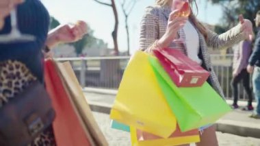 Women drinking traditional aperol spritz cocktail while walking across the city centre street, stylish females with shopping bags enjoying their weekend shopping day in the downtown, fashion models