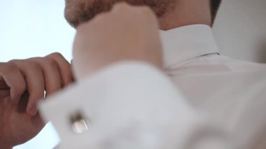 Young handsome businessman preparing for official meeting on corporate party, man in white elegant shirt adjusting black bow tie and looking in the mirror, successful and stylish businessman
