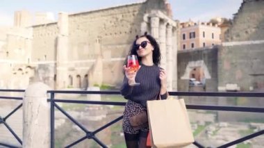 Çekici esmer kadın elinde bir bardak ferahlatıcı portakal kokteyli ile kameraya poz veriyor. Eski Roma mimarisine karşı çekici bir bayan turist. Moda kadını alışveriş yapıyor.